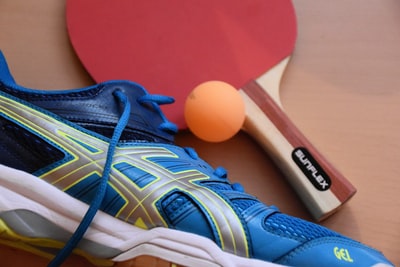 Blue and black ASICS running shoes is near the table tennis racket and ball
